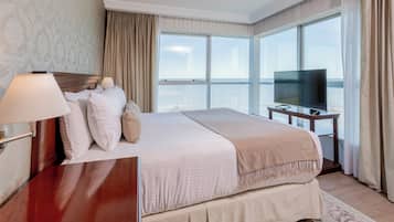 Habitación de hotel con una cama grande, televisor y vistas a la ciudad a través de amplios ventanales.
