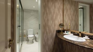 A modern bathroom with a marble floor, a white sink, a large mirror, and a glass shower enclosure.