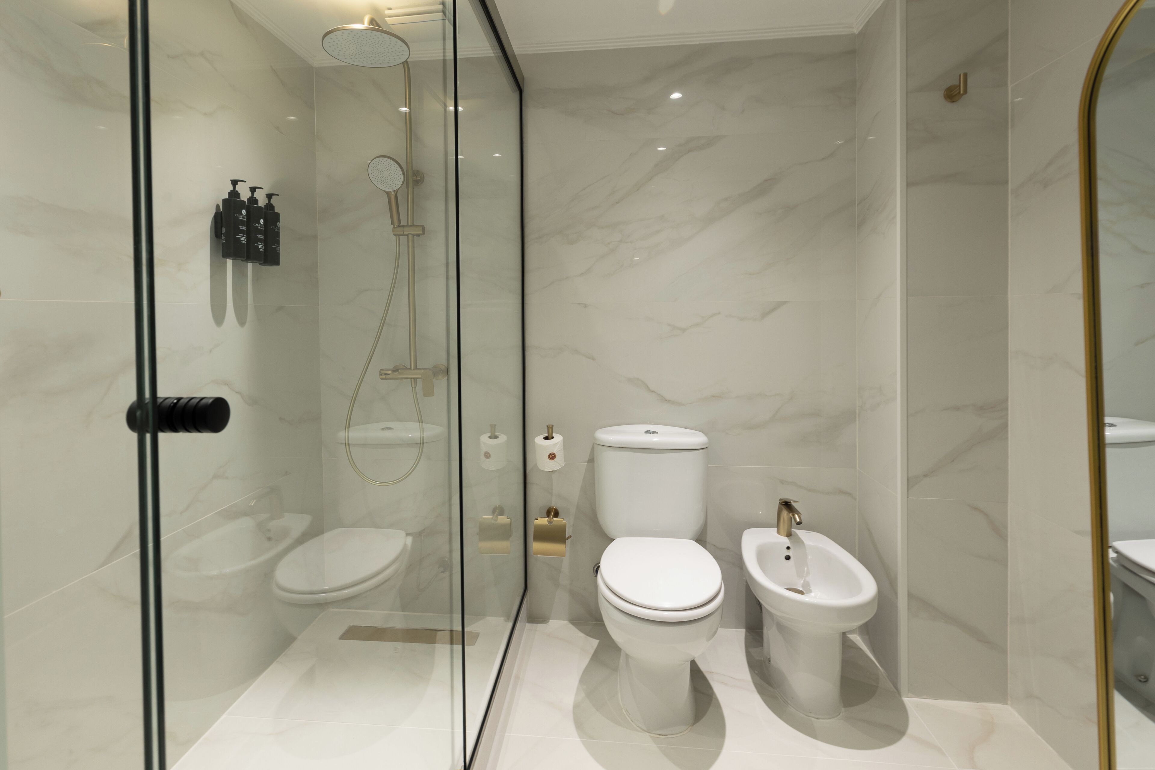 Un baño moderno con ducha de vidrio, inodoro, bidé y paredes de mármol.