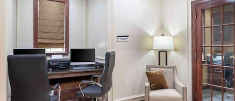 A business center with a desk, two chairs, a lamp, and a sign indicating 24-hour business center availability.