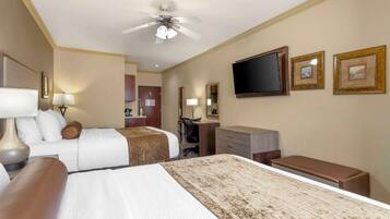 A hotel room with two beds, a desk, a chair, a television, and a ceiling fan.