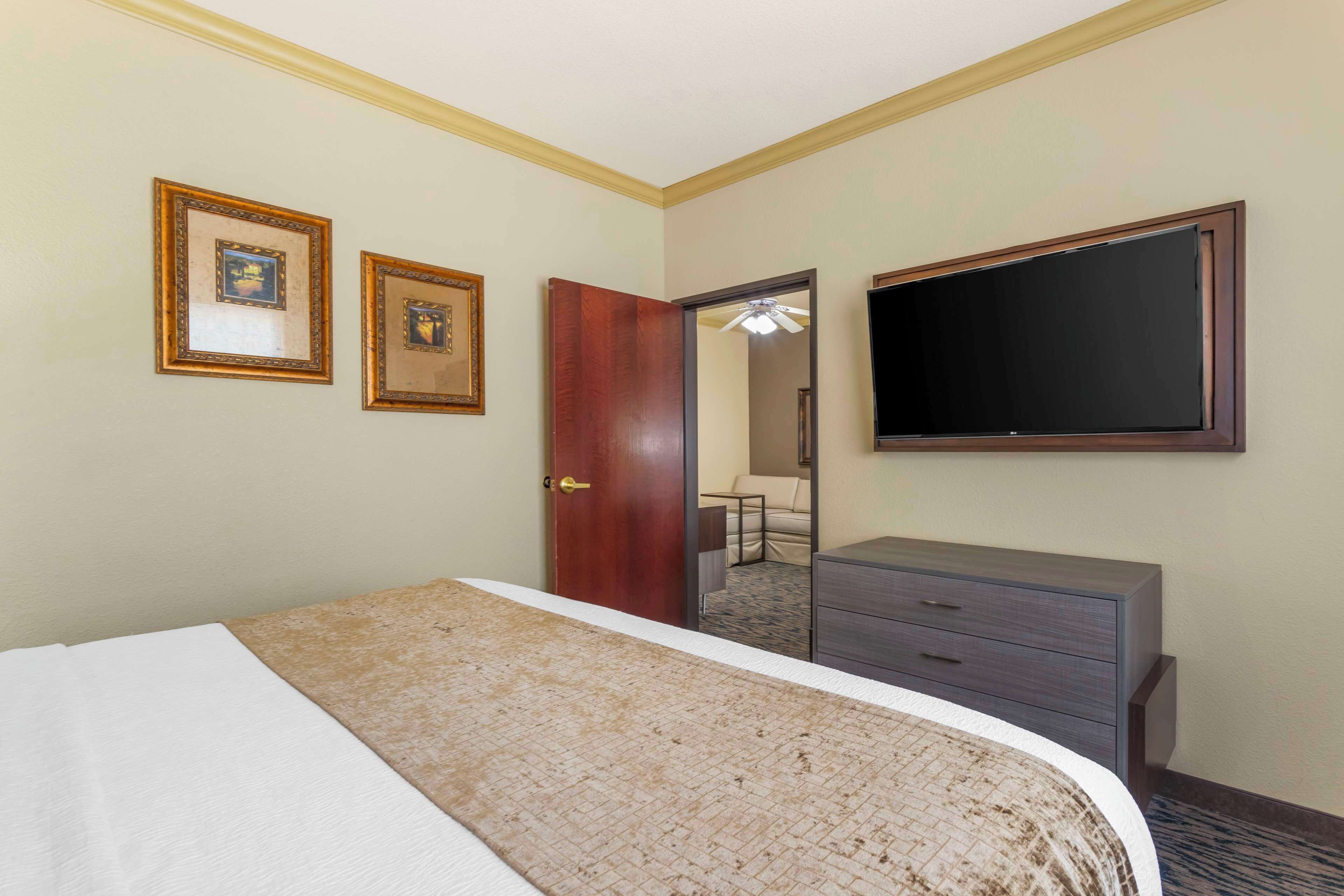A hotel room with a bed, a dresser, a flat-screen TV, and two framed pictures on the wall.