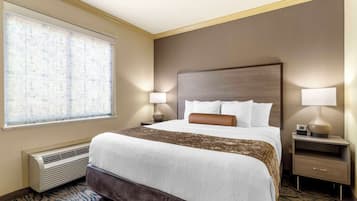 A hotel room with a large bed, two bedside tables with lamps, a window with blinds, and a wall-mounted heater.