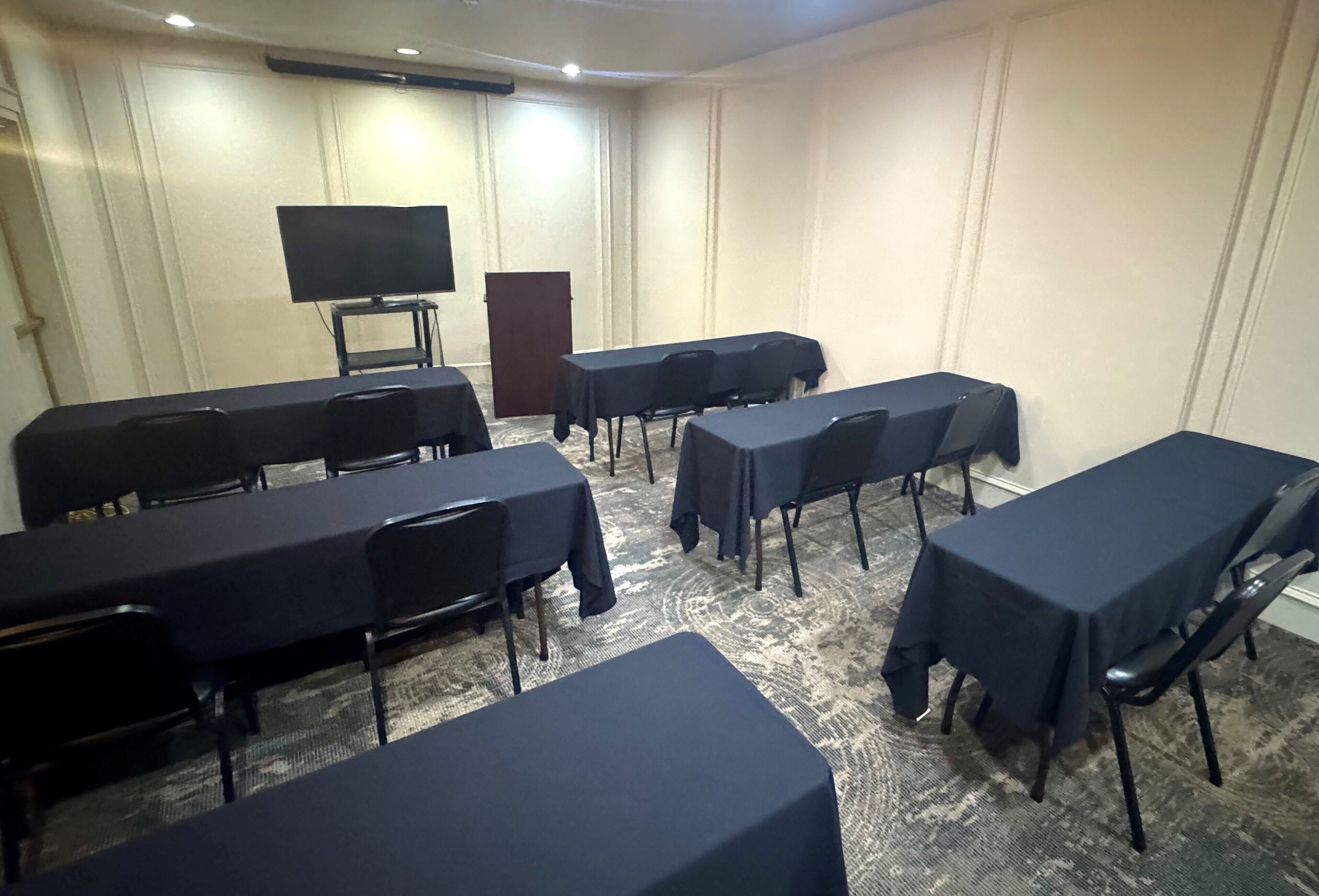 Una sala conferenze con diversi tavoli e sedie, un televisore su supporto e un podio.