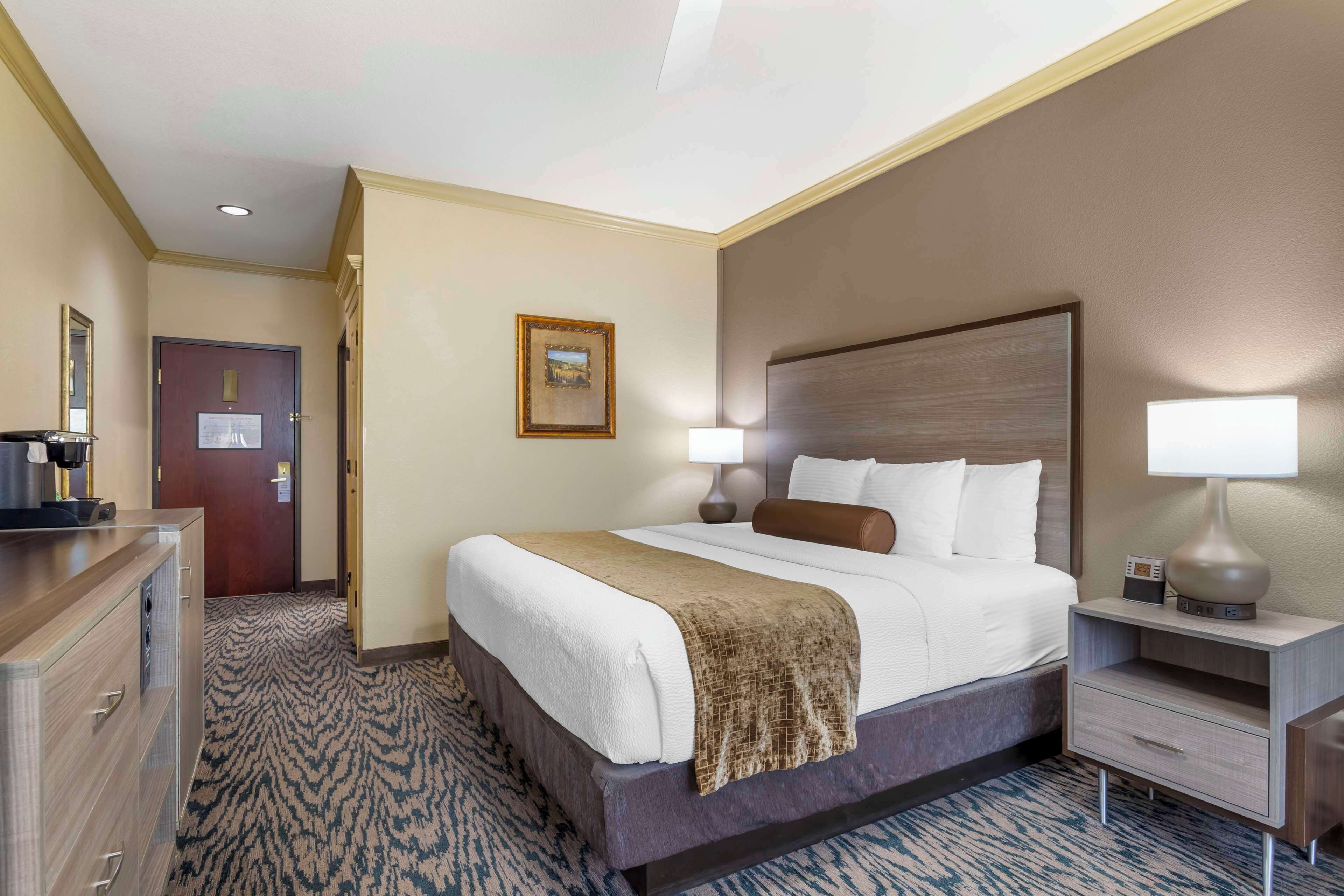 A hotel room with a large bed, bedside lamps, a dresser, a door with a sign, and a framed picture on the wall.
