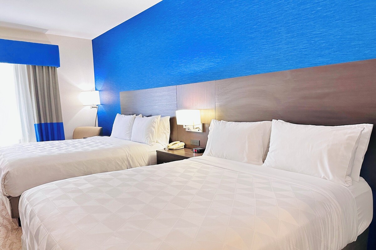A hotel room with two beds, a nightstand with a phone, and a wall with a blue accent.