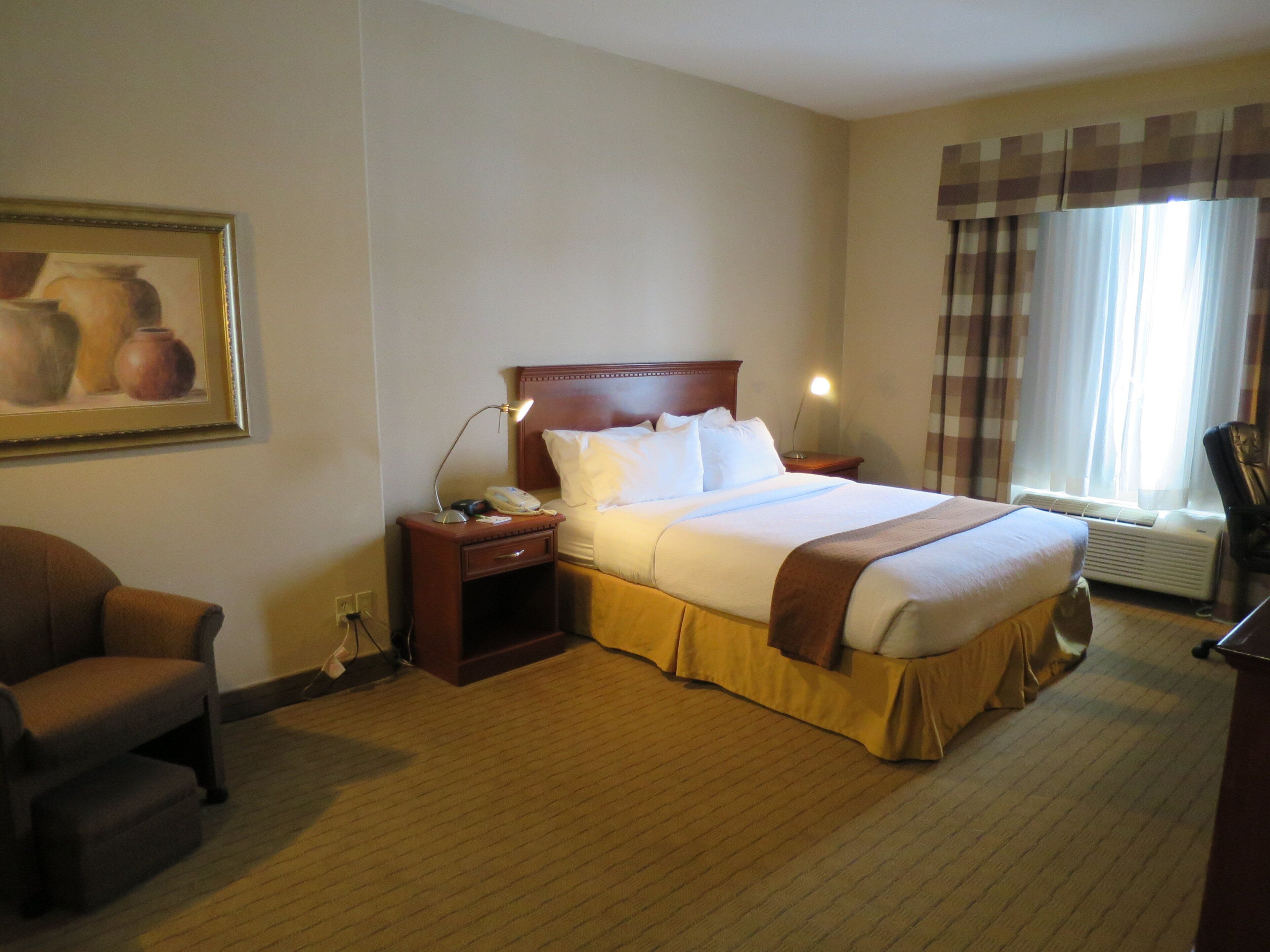 A hotel room with a bed, bedside tables, a lamp, a chair, and a painting on the wall.