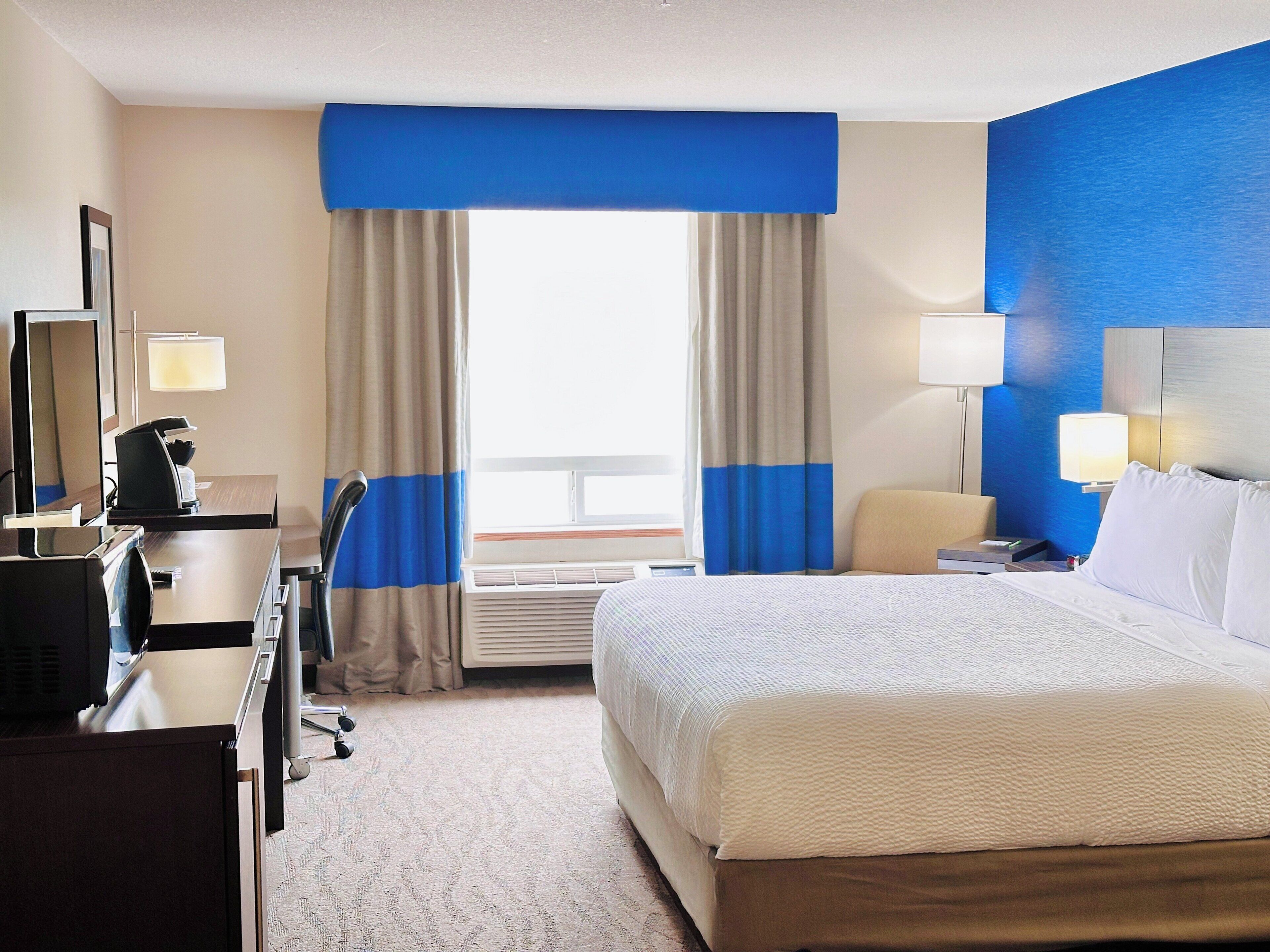 A hotel room with a bed, a desk, a chair, and a window with curtains.