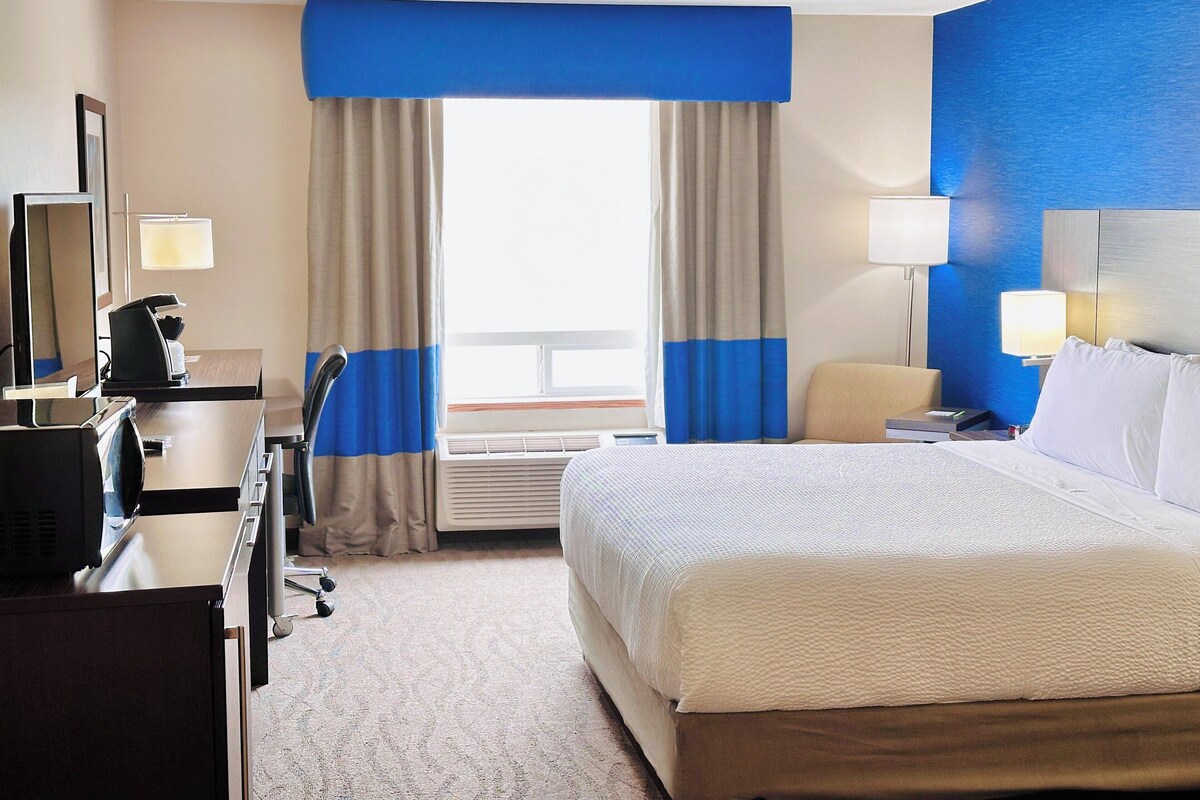 A hotel room with a bed, a desk, a chair, and a window with curtains.