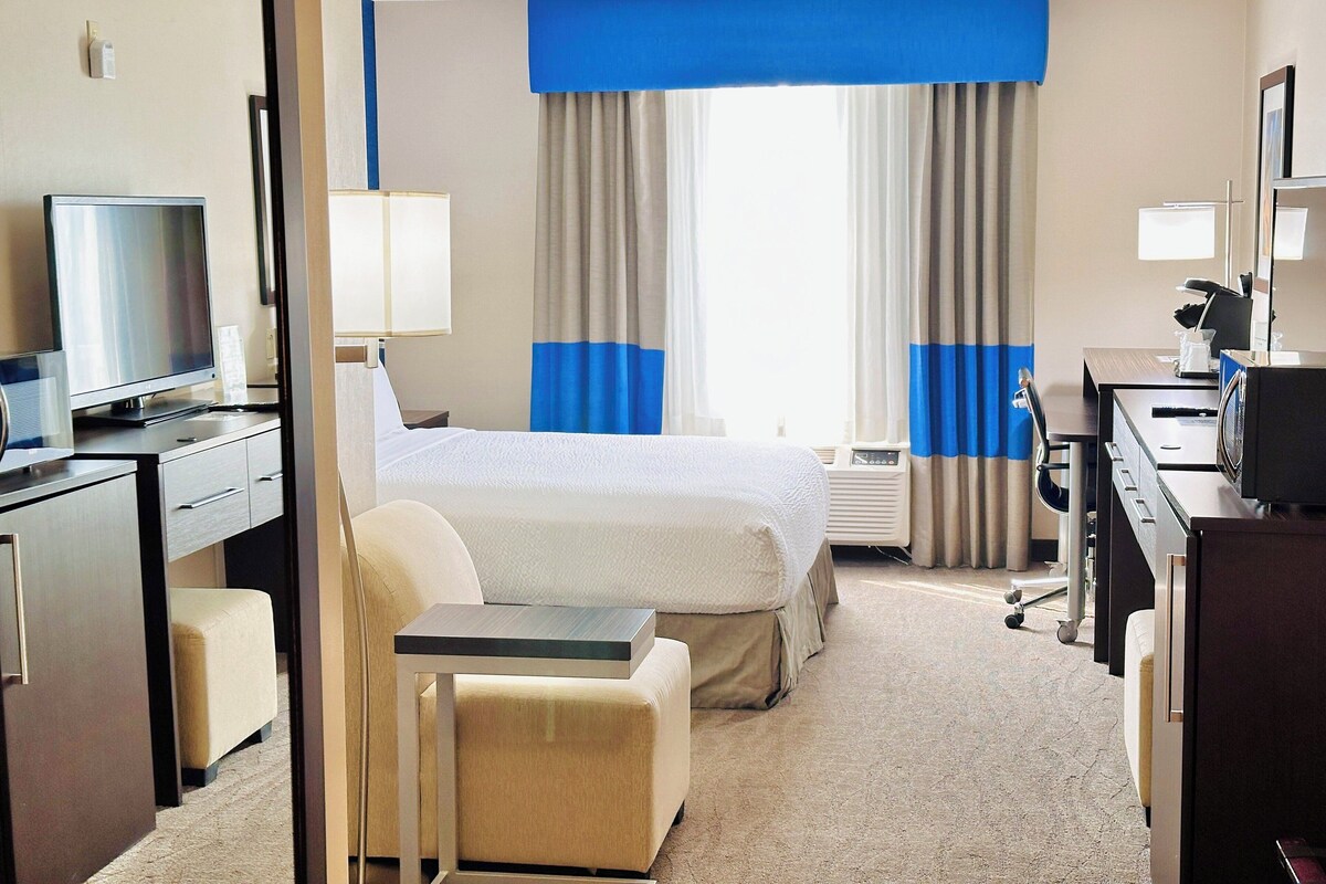 A hotel room with a bed, a desk, a chair, a television, and a window with curtains.