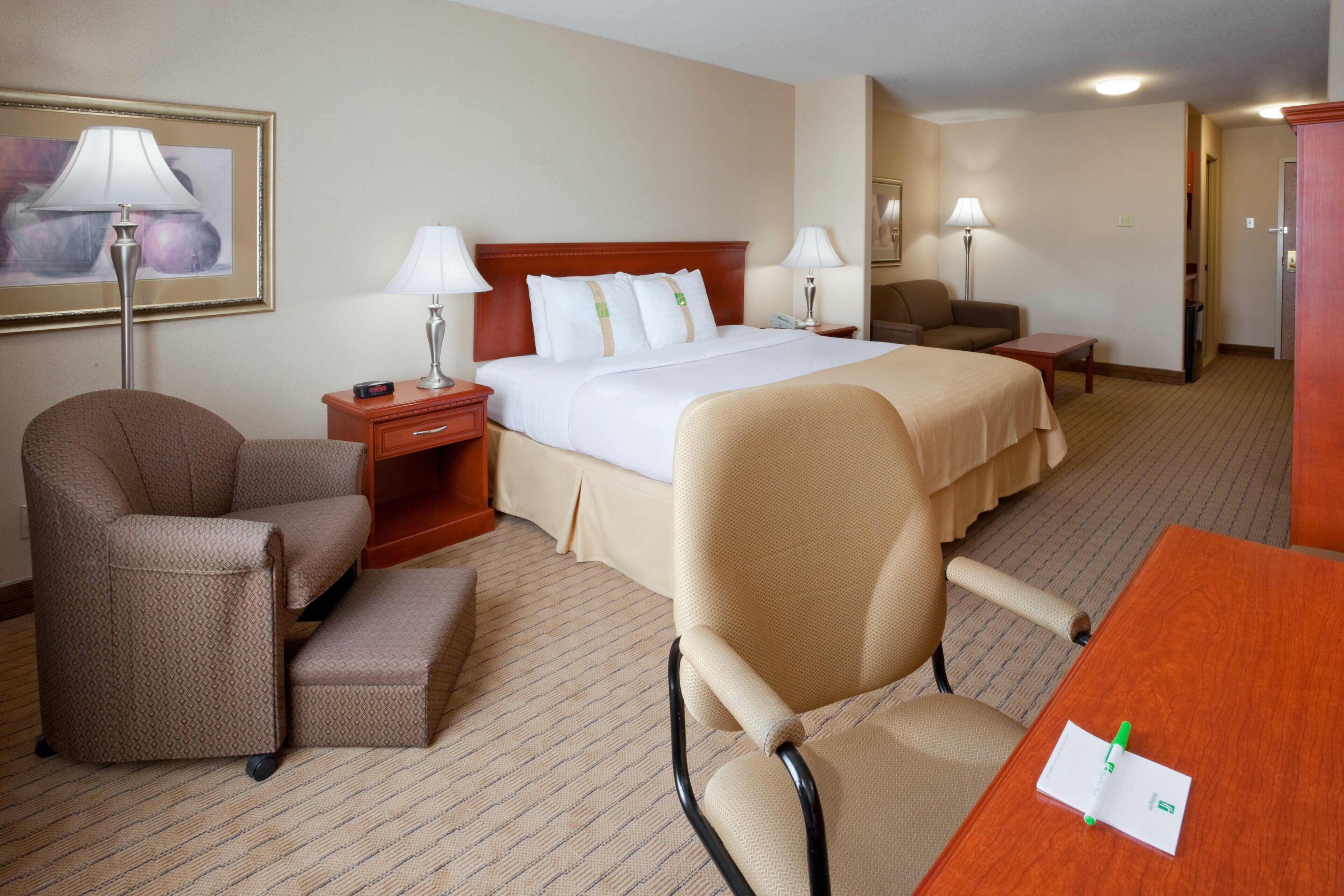 A hotel room with a bed, two bedside tables, a desk, a chair, and a lamp.