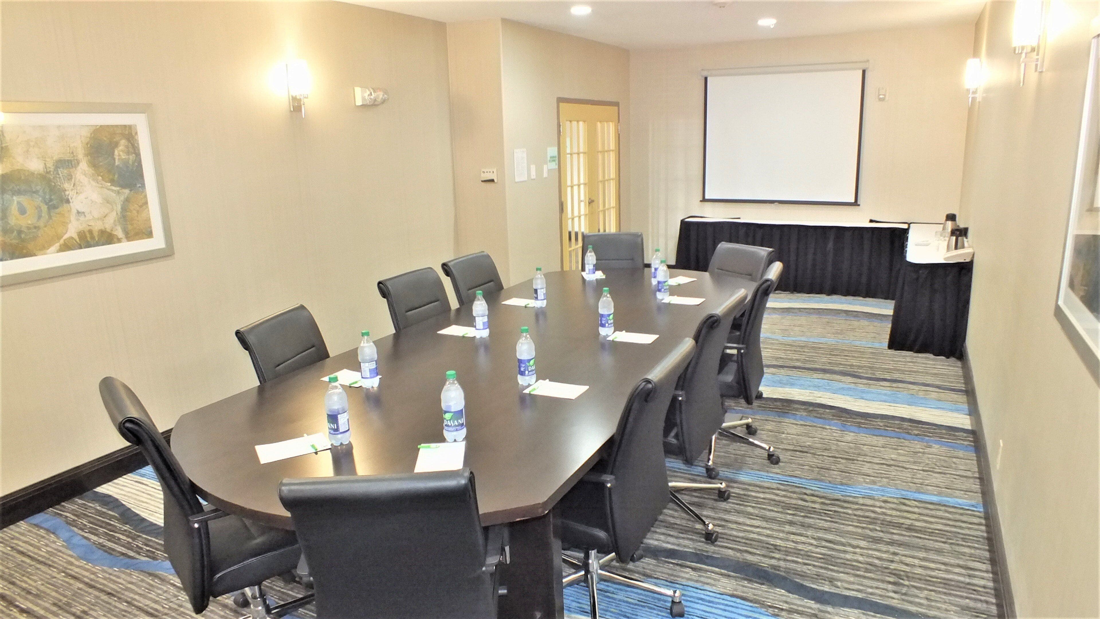 A conference room with a long table, chairs, water bottles, a projector screen, and a presentation screen.