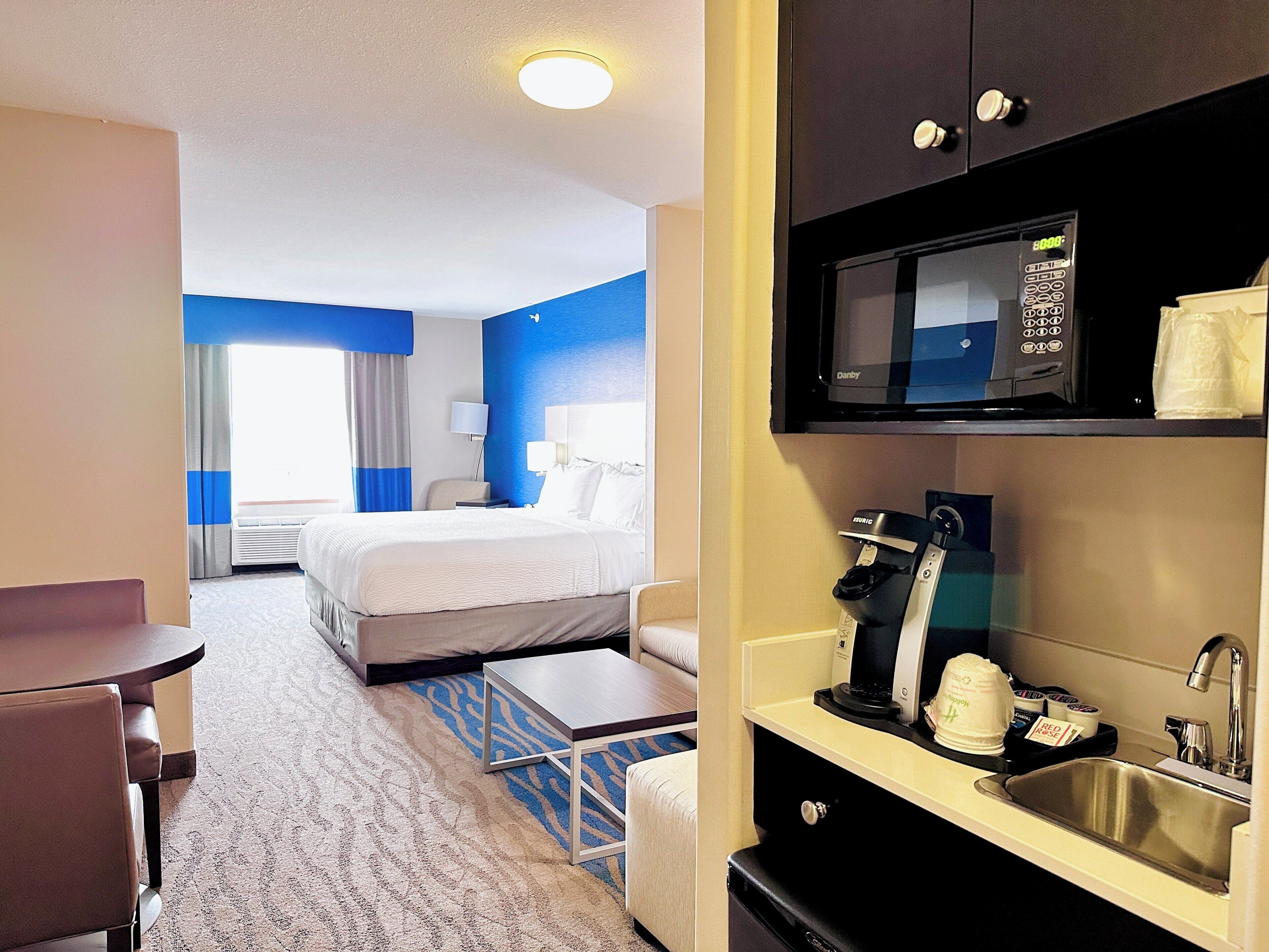 Une chambre d’hôtel équipée d’un lit, d’un bureau, d’une machine à café, d’un four à micro-ondes et d’un lavabo.