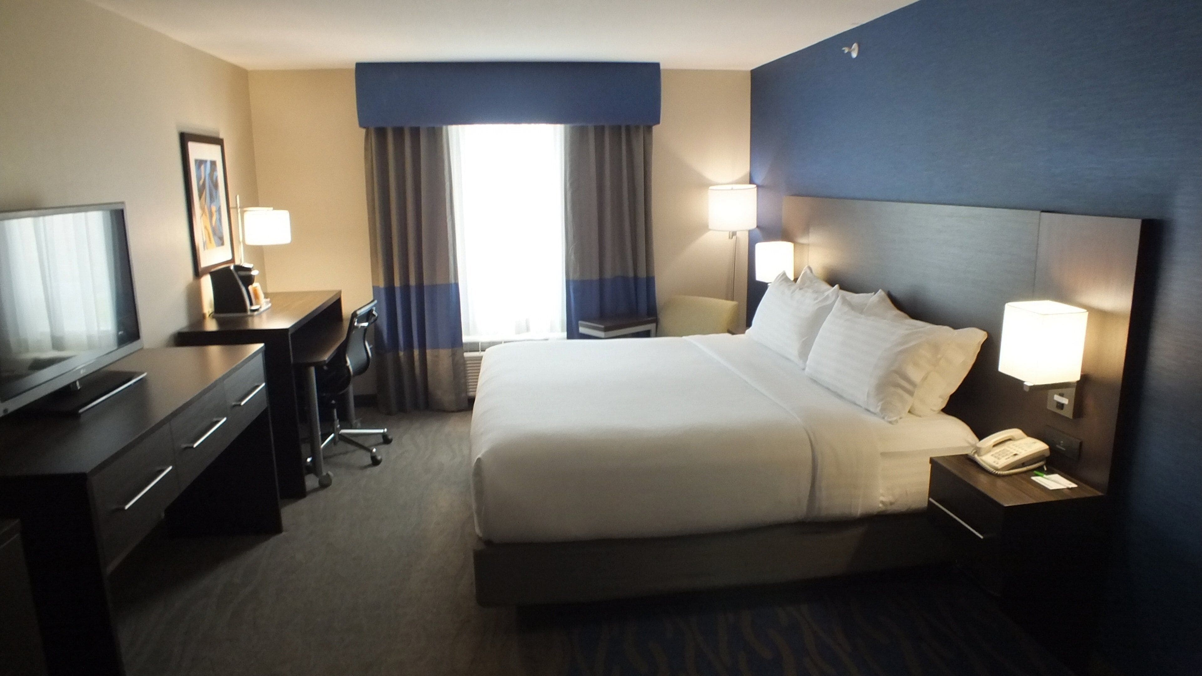 A hotel room with a bed, bedside lamps, a desk with a television, and a window with curtains.