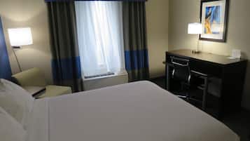 A hotel room with a bed, a desk, a chair, a lamp, and a window with curtains.