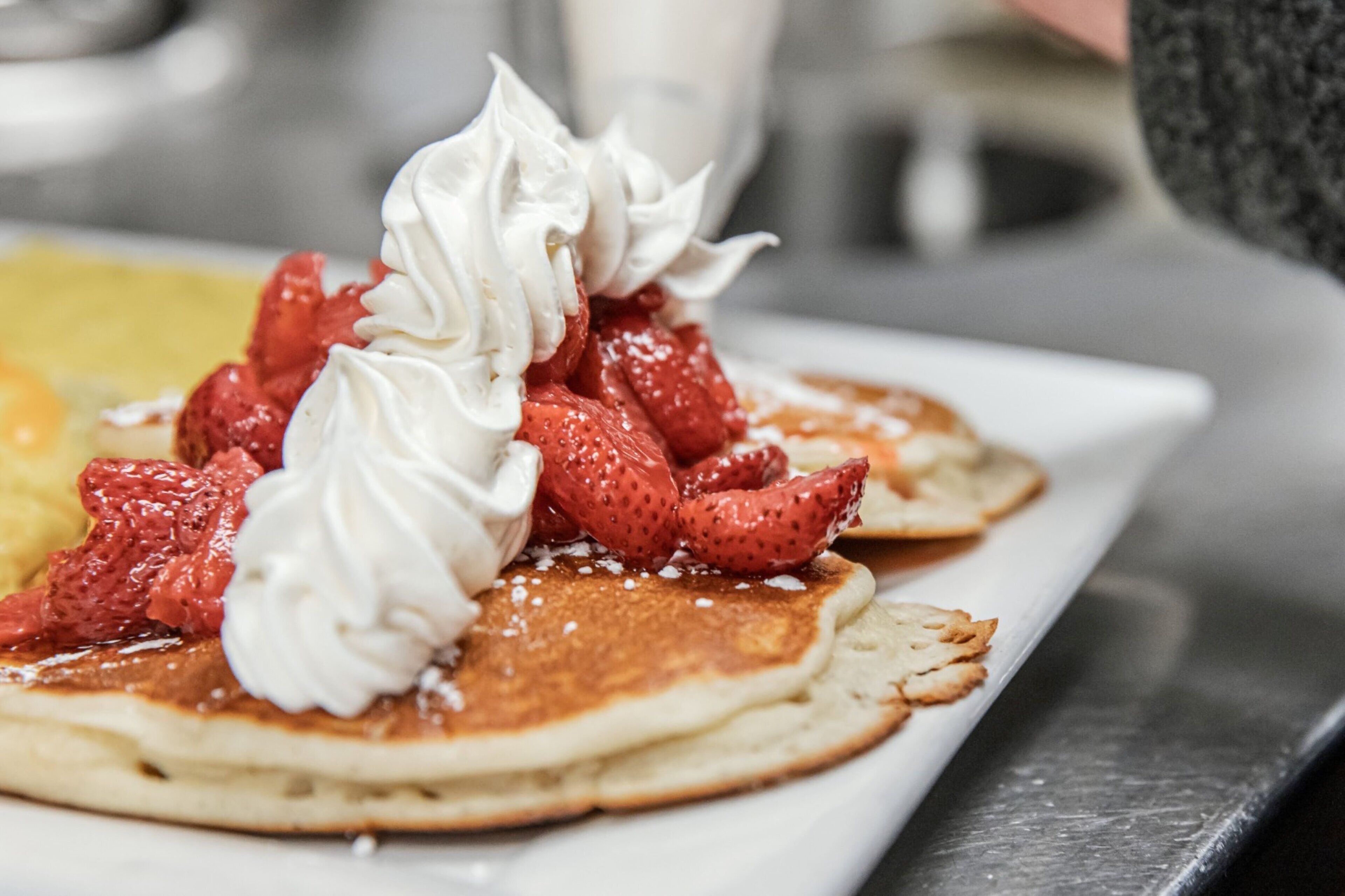 A plate of pancakes topped with whipped cream and strawberries.