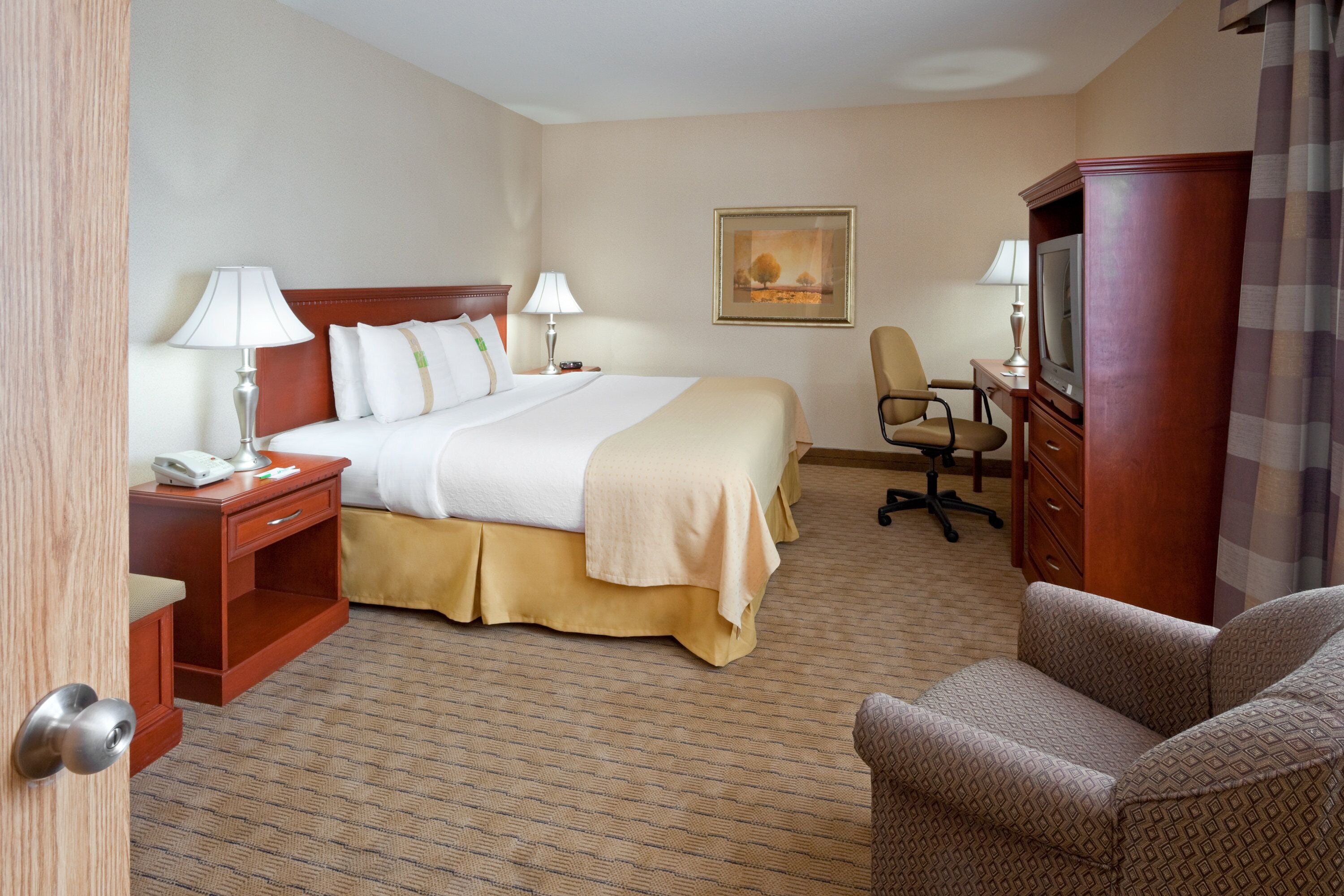 A hotel room with a bed, bedside tables, a desk with a chair, a television, and a painting on the wall.