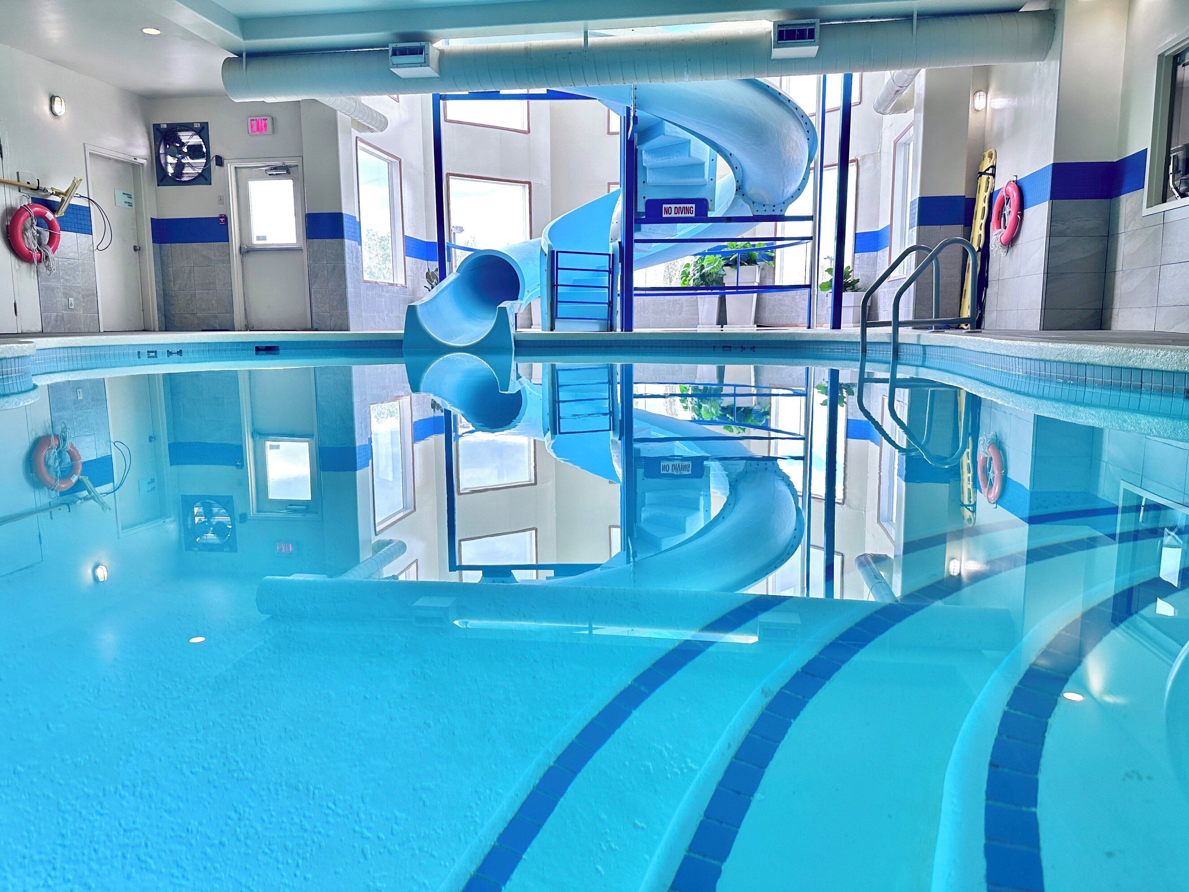 Une piscine avec un toboggan bleu en forme de spirale, une eau claire et du matériel de sécurité.