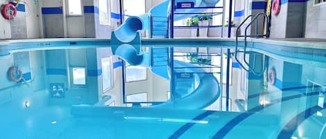A swimming pool with a blue spiral slide, clear water, and safety equipment.