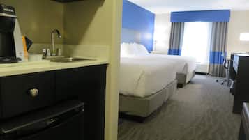 Quarto de hotel com cozinha compacta, uma cama, escrivaninha e janela com cortinas.
