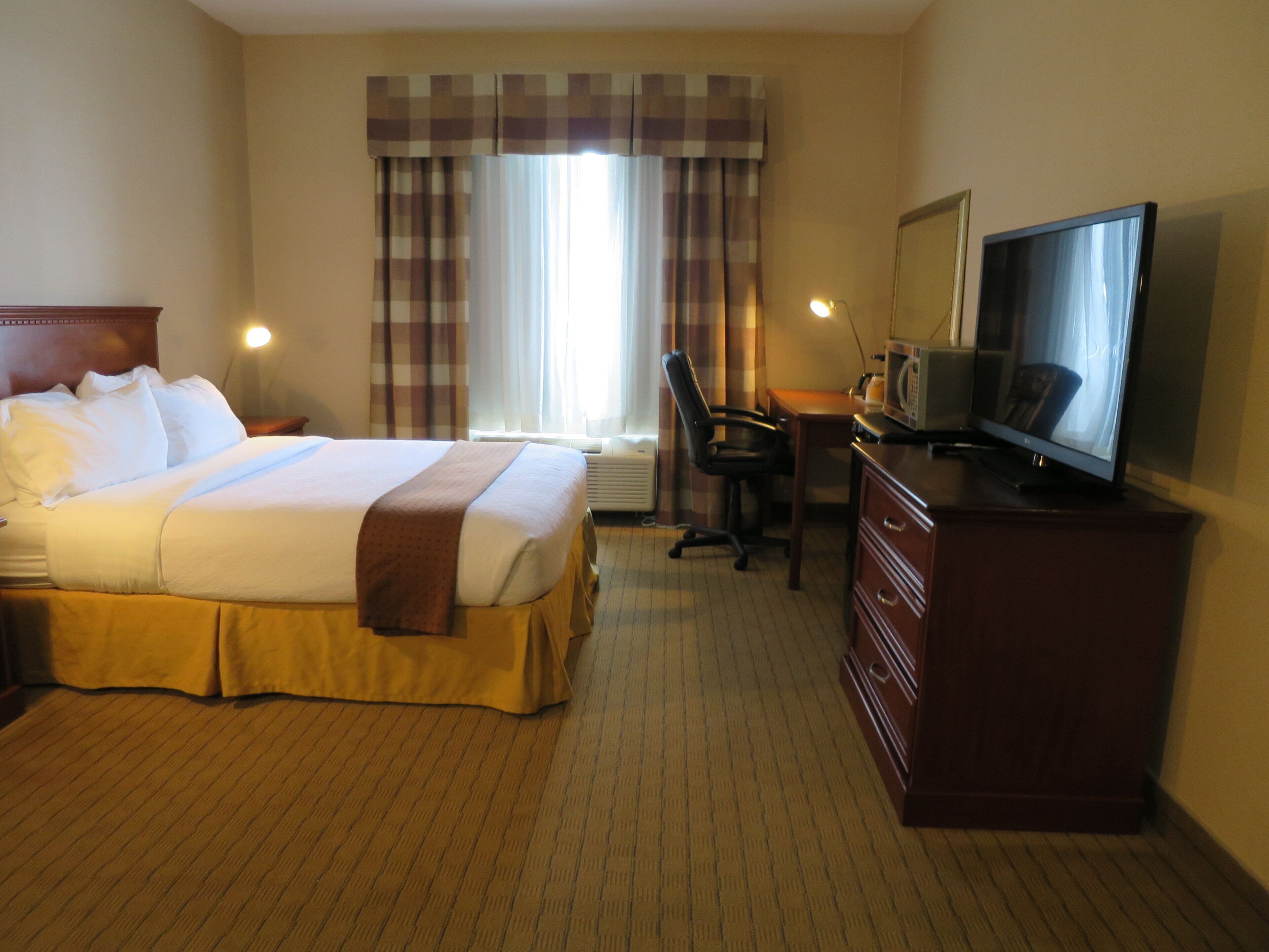 Een hotelkamer met een bed, bureau, stoel, televisie en een dressoir.