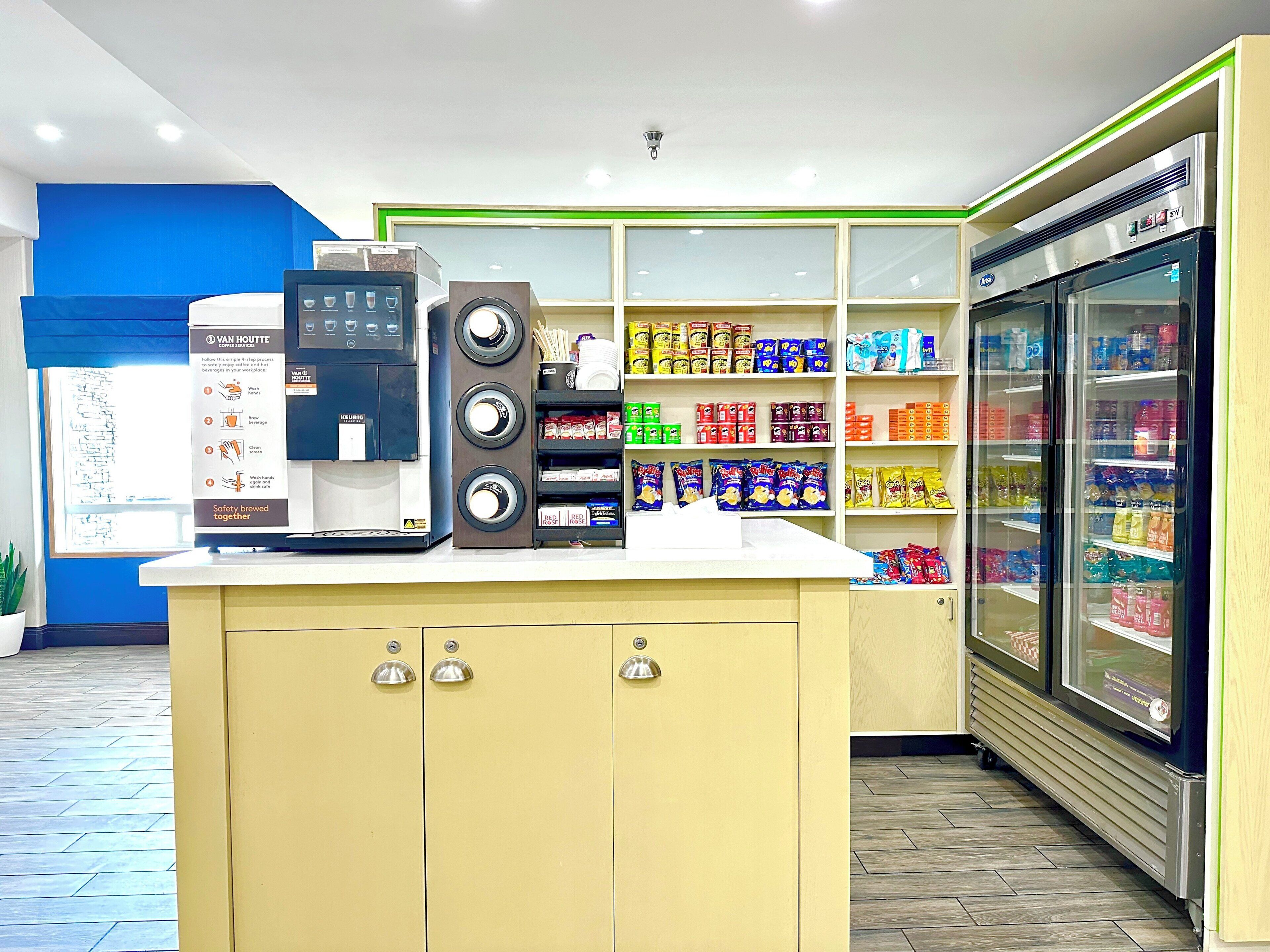 A coffee machine, snack shelves, and a refrigerator in a modern kitchen area.
