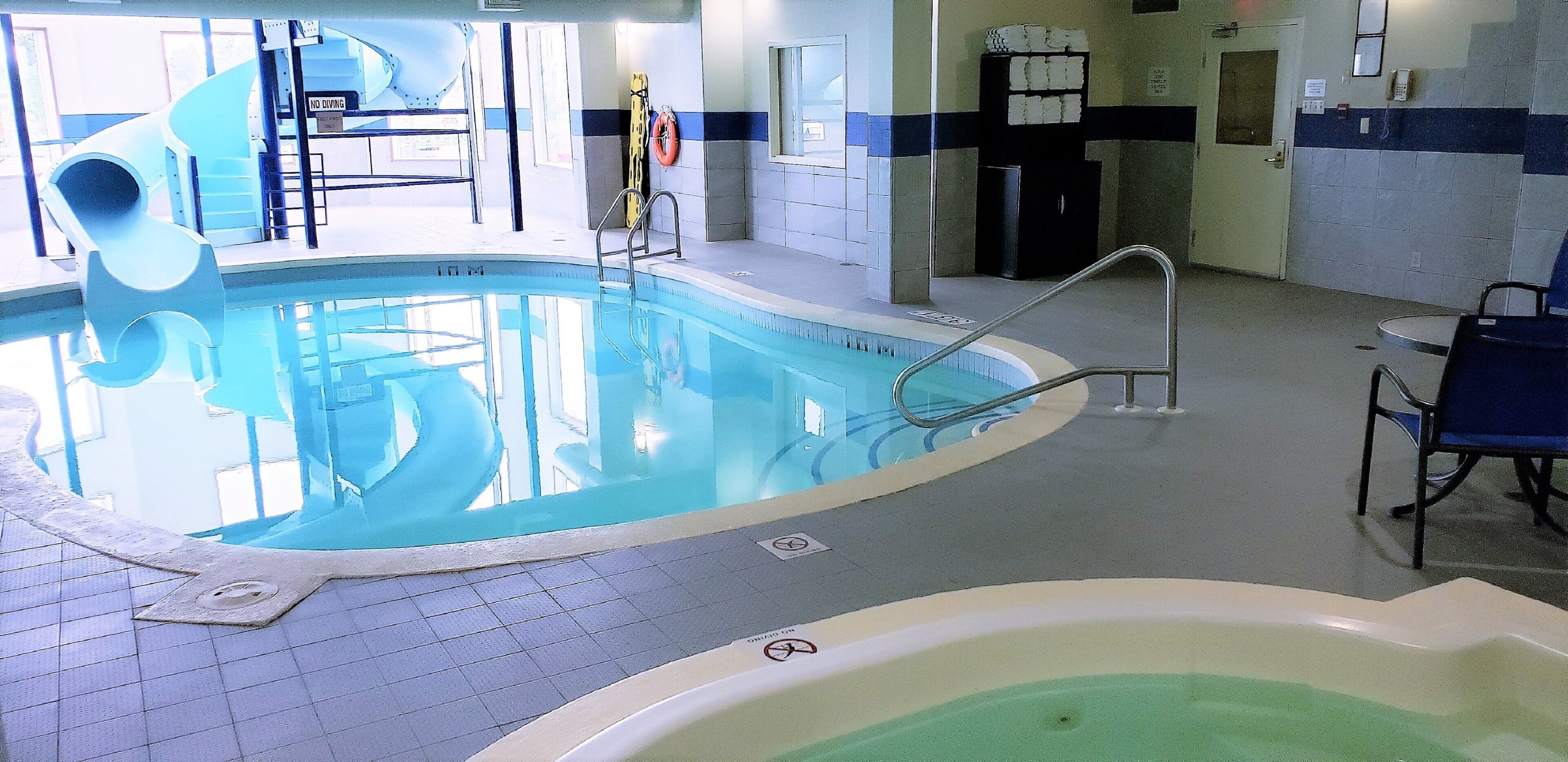 An indoor swimming pool with a no diving sign, a lifebuoy, and a pool ladder.