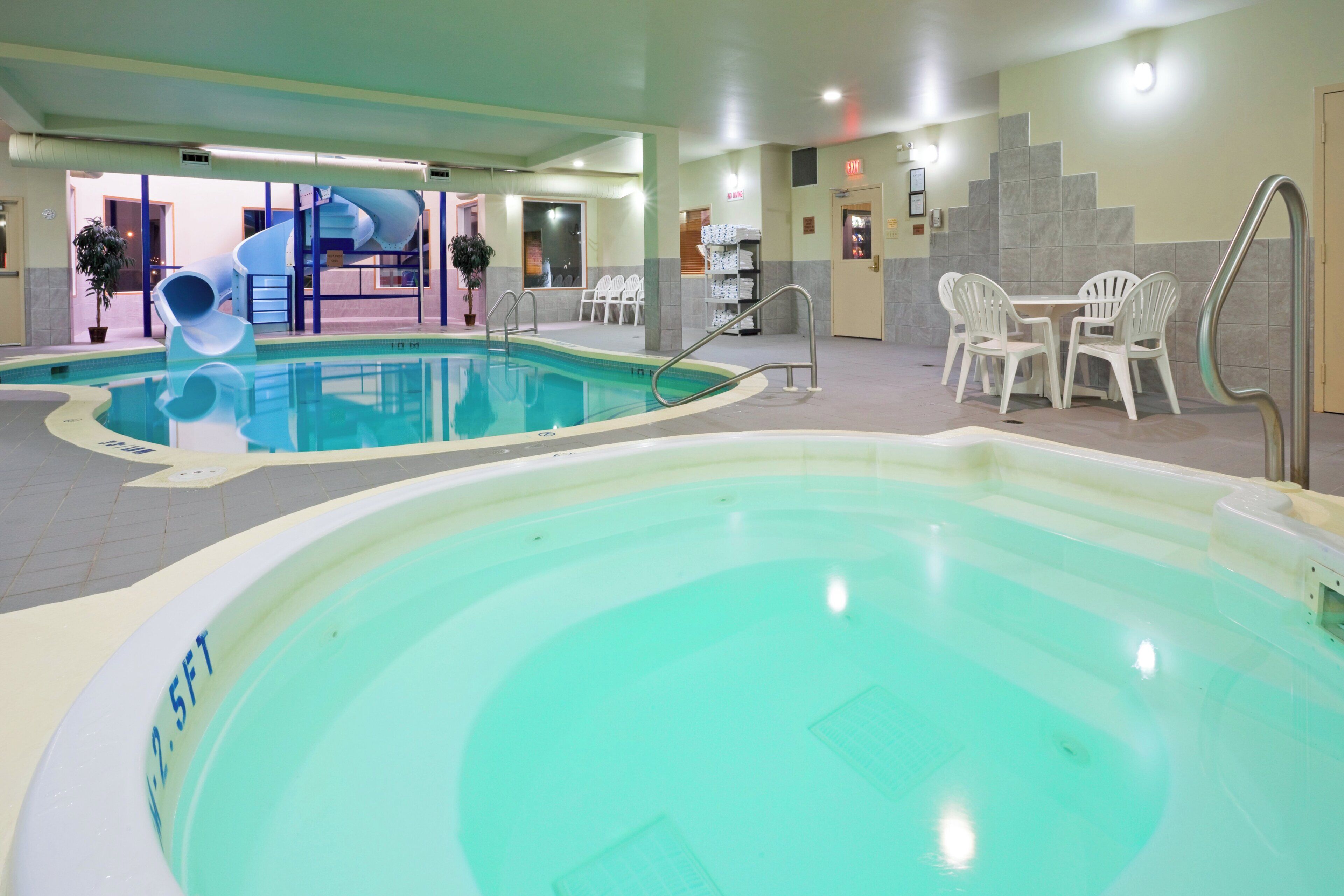 An indoor swimming pool with a slide, seating area, and a small table.