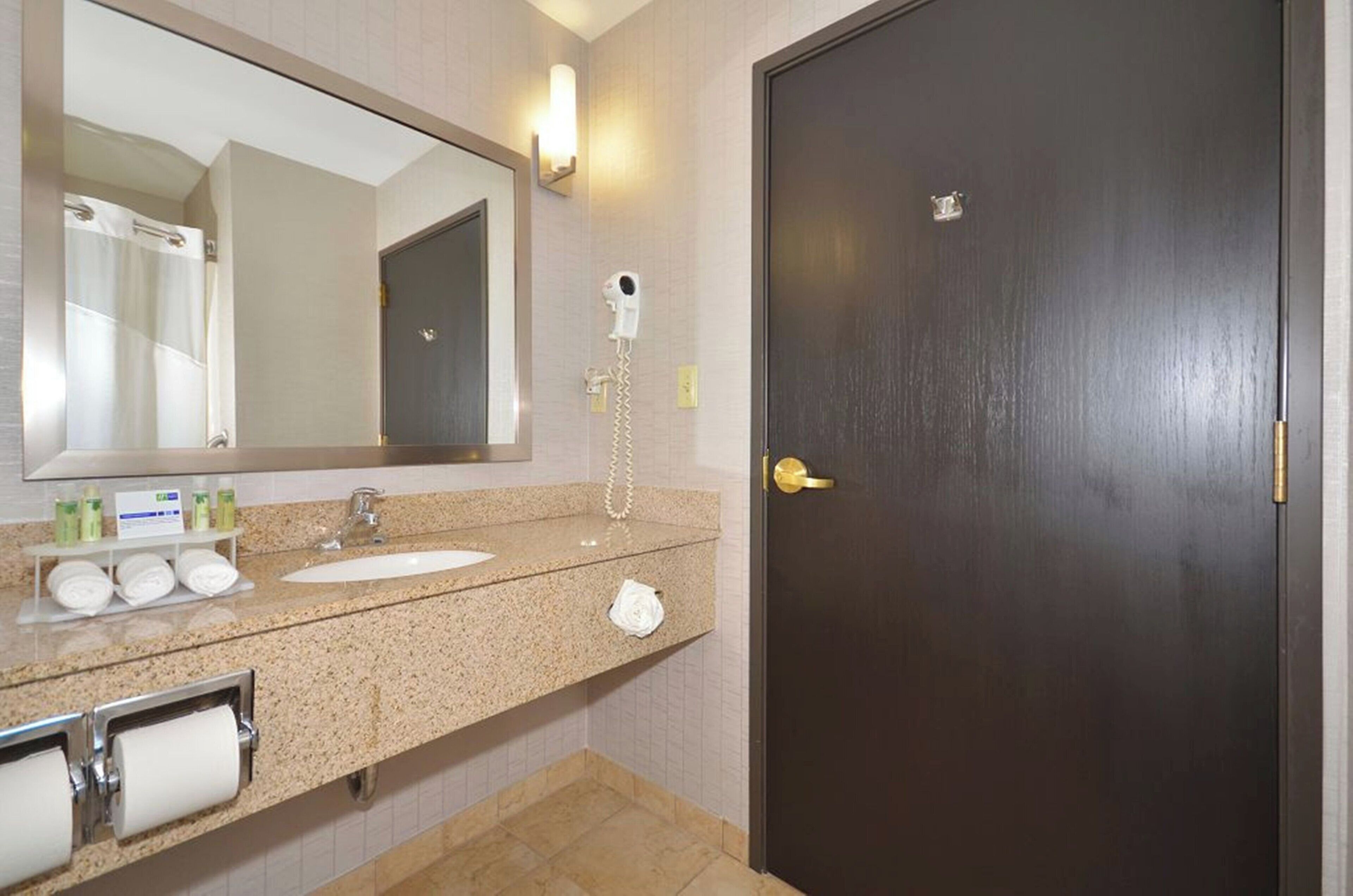 Une salle de bain avec une porte sombre, un lavabo, un miroir et un sèche-cheveux.