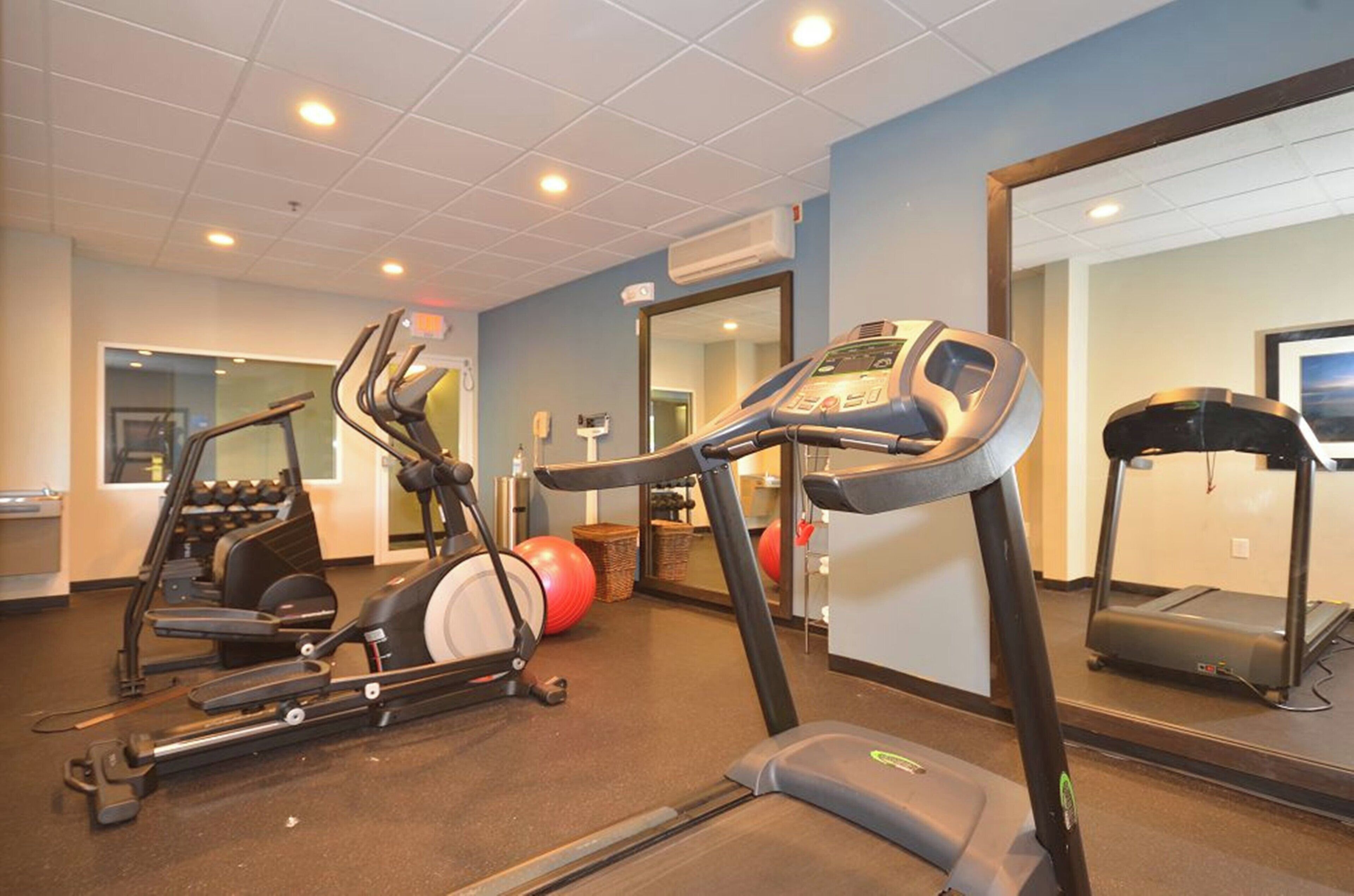 A gym with treadmills, elliptical machines, and exercise balls.