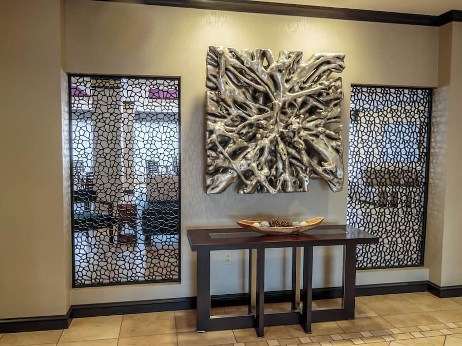 A reception area with a modern design, featuring a decorative wall piece, a small table with a bowl, and a patterned partition.