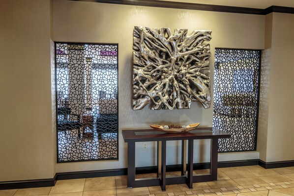 A reception area with a modern design, featuring a decorative wall piece, a small table with a bowl, and a patterned partition.