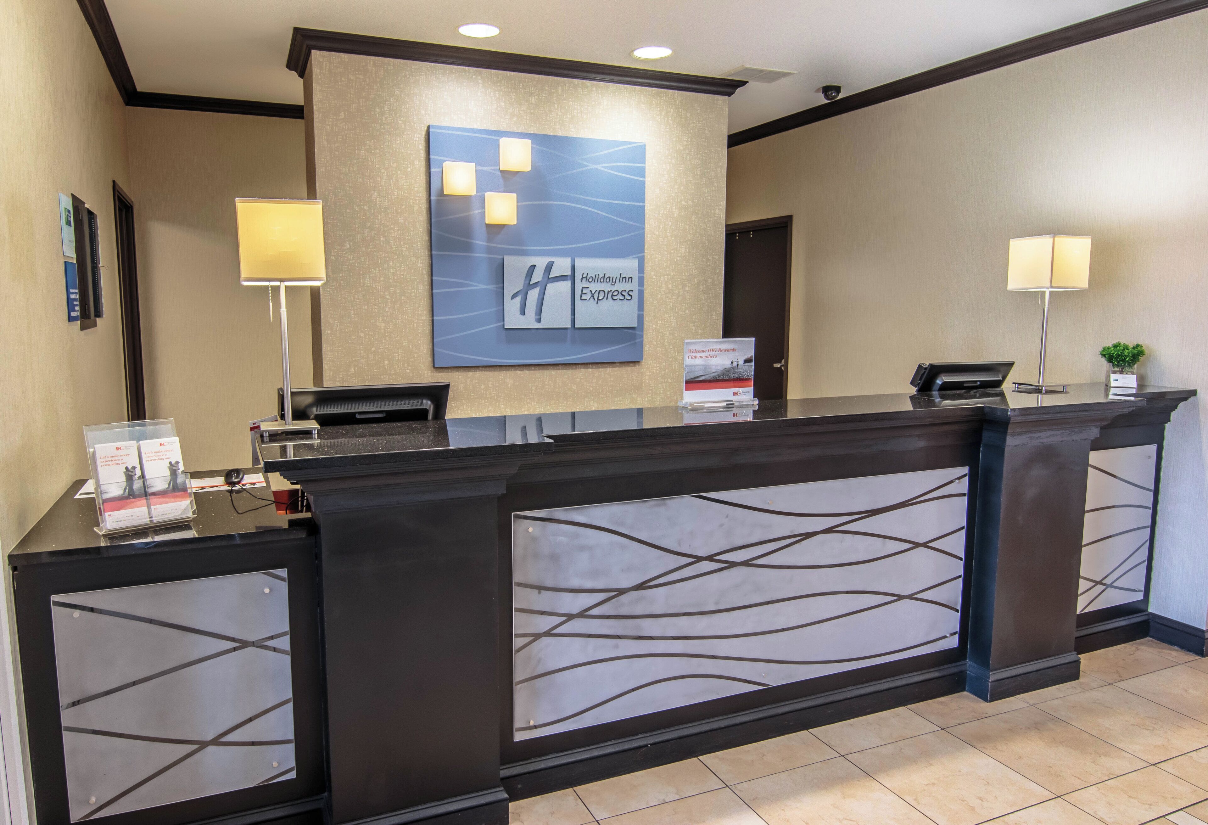 A hotel reception desk with a modern design, including a large logo and a welcome sign for Holiday Inn Express.
