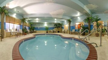 Piscina interior com borda azulejada, rodeada por espreguiçadeiras e plantas em vasos.
