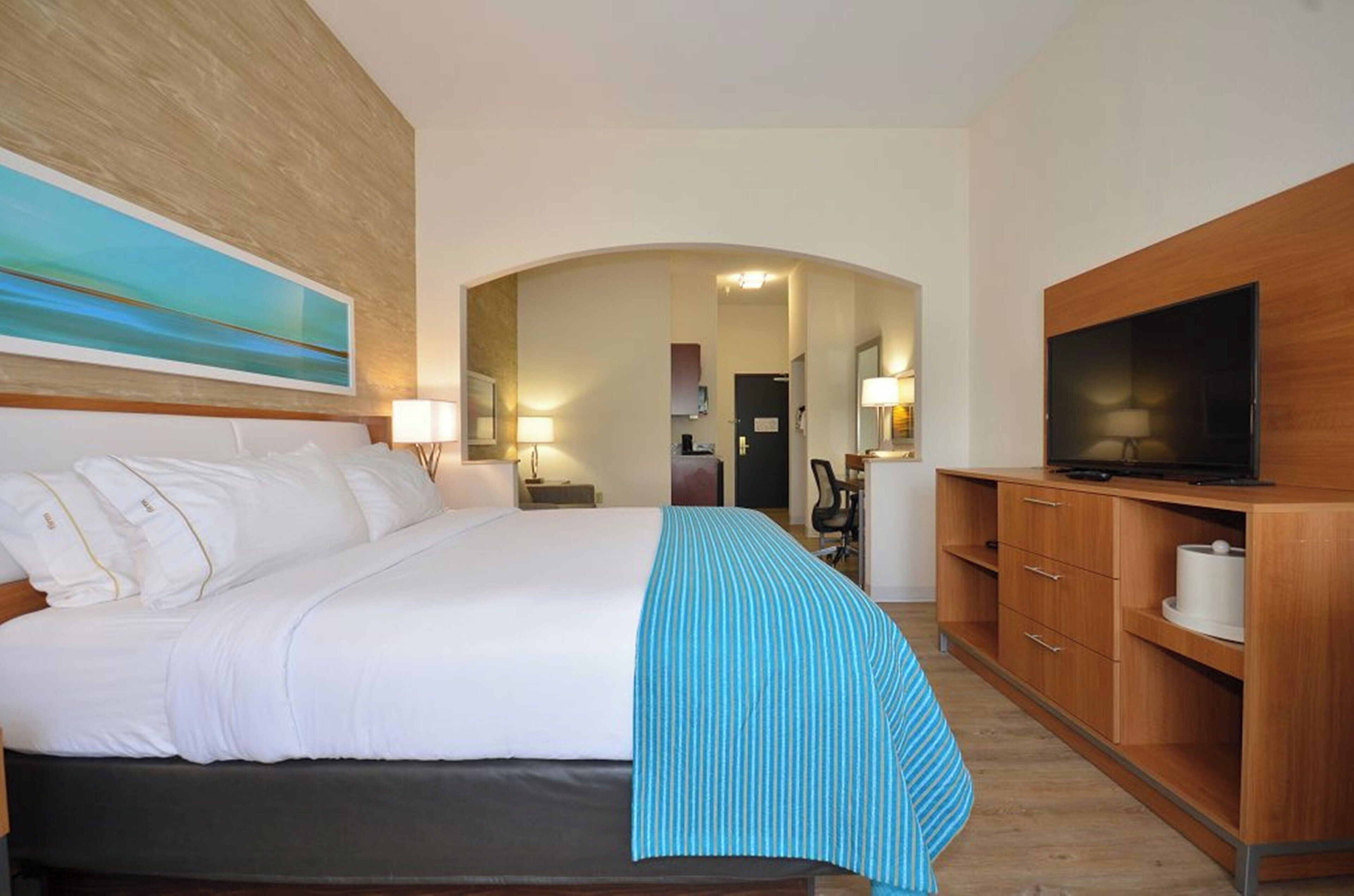 A hotel room with a bed, a television, a desk, and a bathroom visible through an archway.