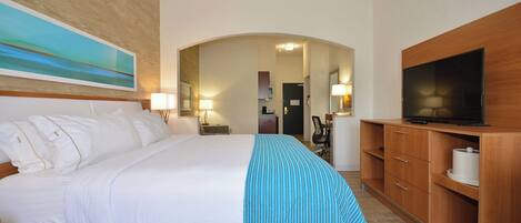 A hotel room with a bed, a television, a desk, and a bathroom visible through an archway.