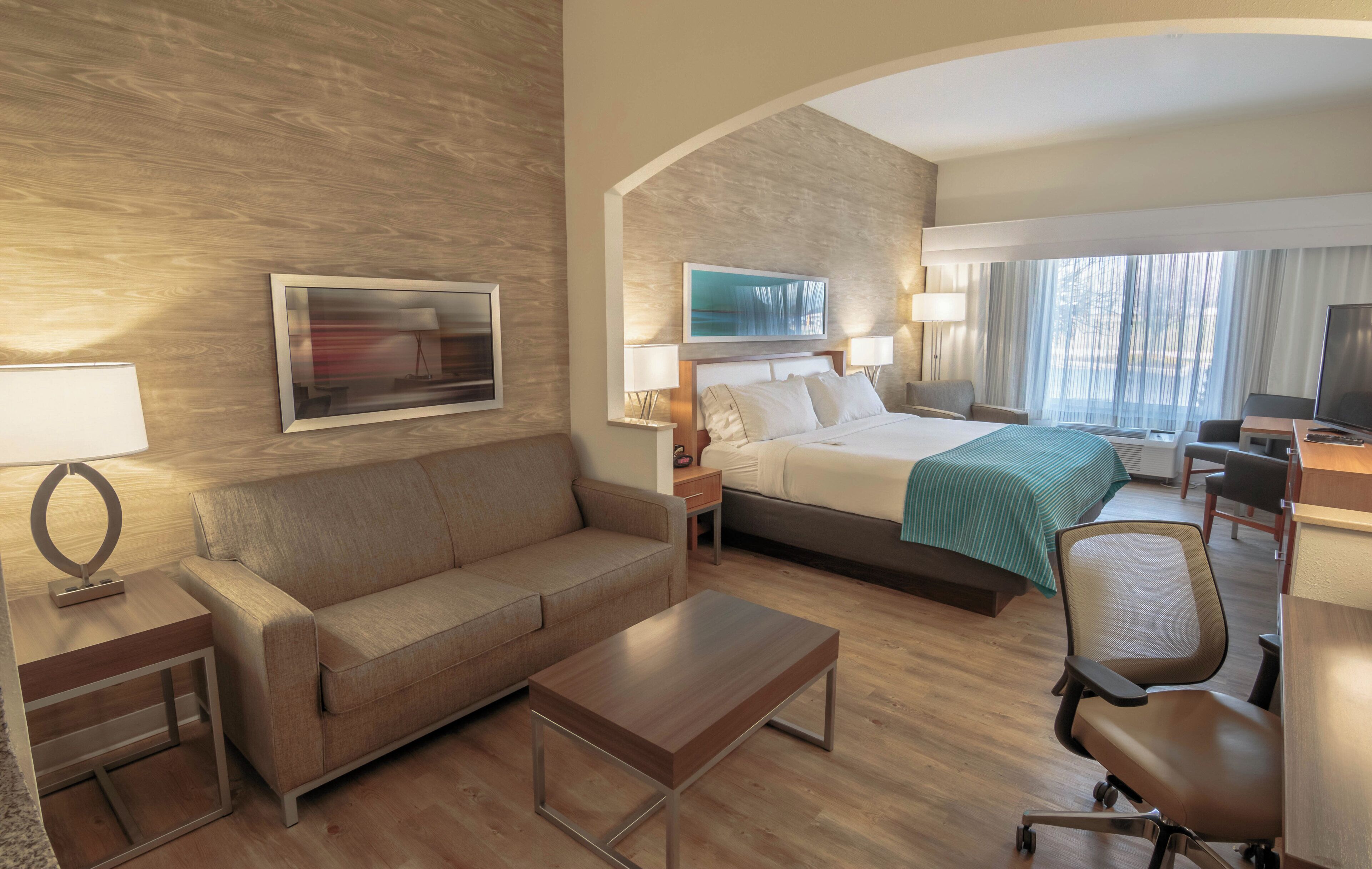 Ein Hotelzimmer mit einer Couch, einem Bett, einem Schreibtisch, einem Sessel und einem Fernseher.
