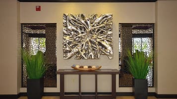 Uma área de recepção com arte de parede abstrata moderna, duas plantas em vasos e um console de madeira com uma tigela decorativa.