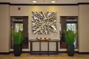 A reception area with a modern abstract wall art, two potted plants, and a wooden console table with a decorative bowl.