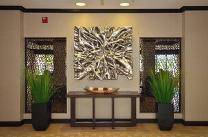 Zona de recepción con un cuadro abstracto moderno, dos plantas en macetas y una consola de madera con un cuenco decorativo.