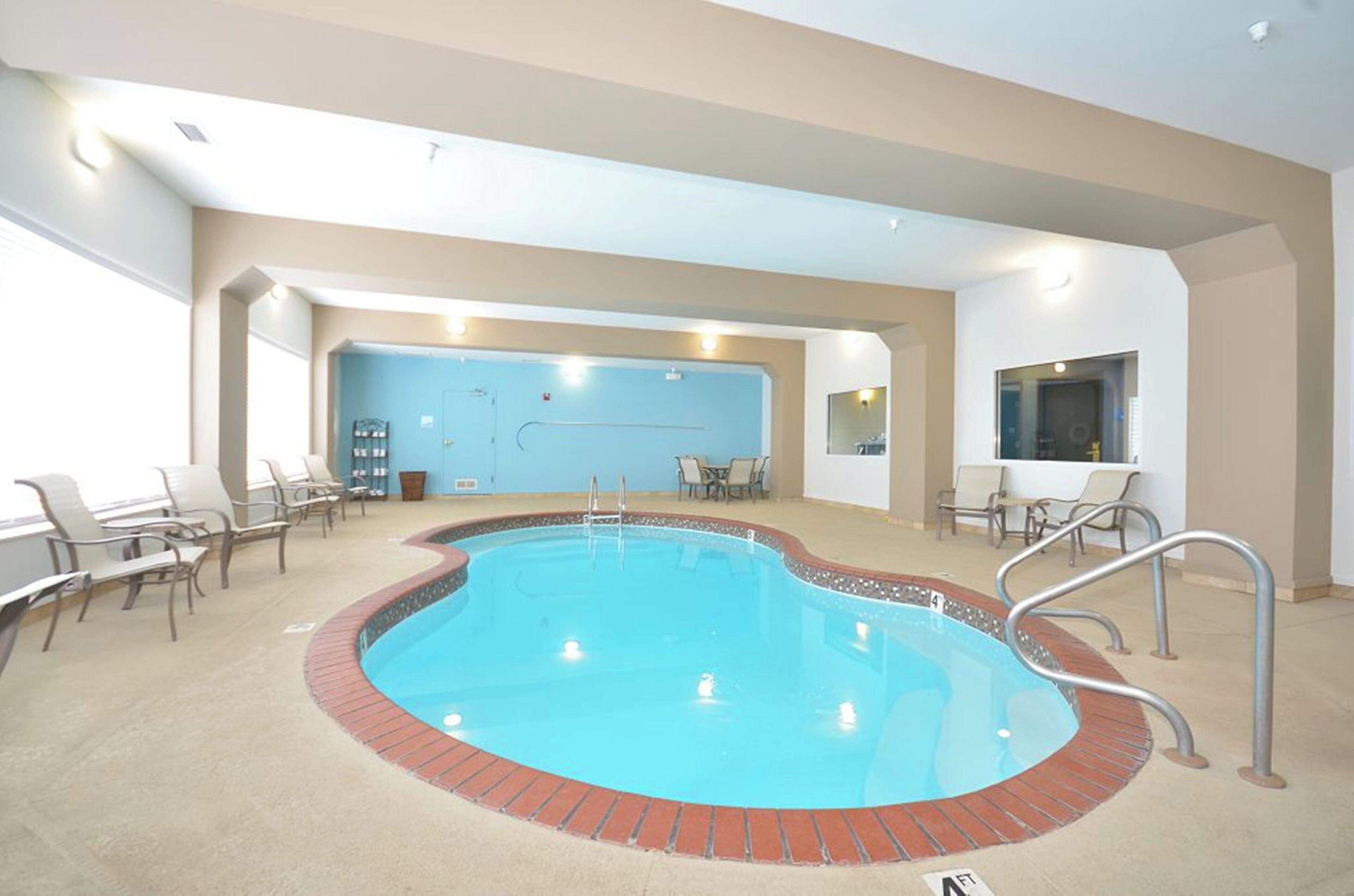 An indoor swimming pool with a brick edge, surrounded by lounge chairs and a seating area.