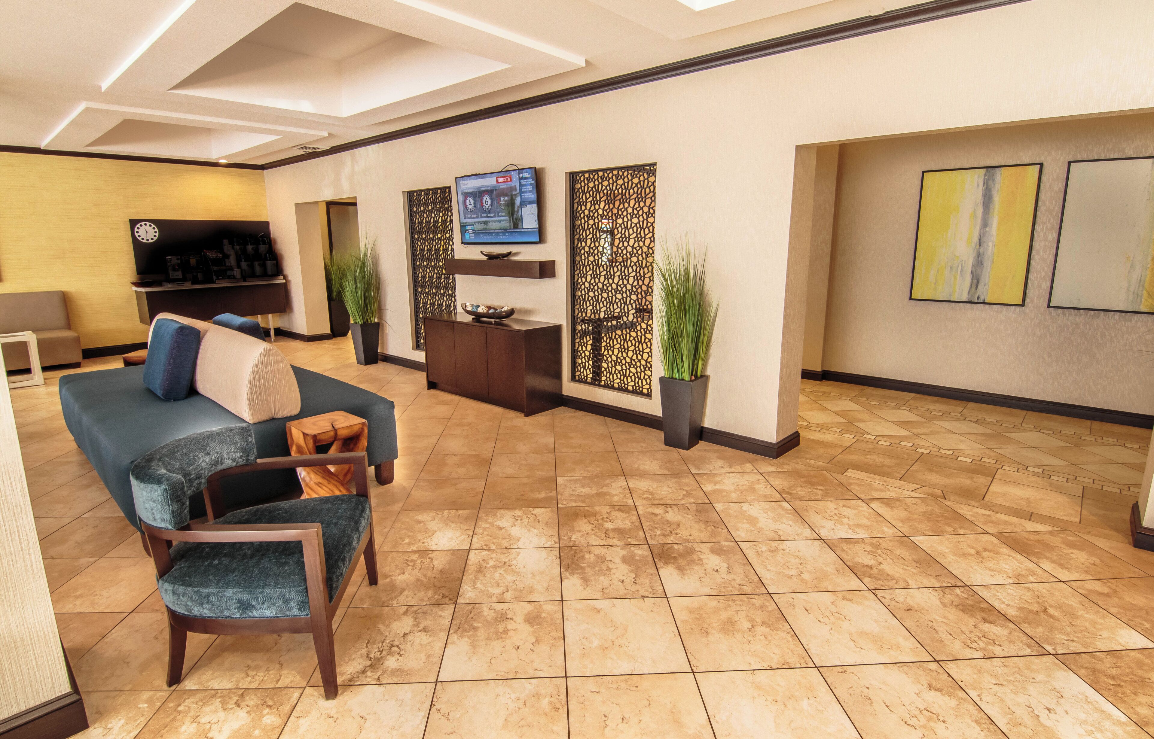 A modern lobby with a sofa, chairs, a TV, decorative panels, and a reception desk.