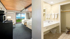 Une chambre d’hôtel avec un plafond en bois, un grand lit, une vue sur la mer, une salle de bain avec un lavabo et un miroir, et un panier à linge.