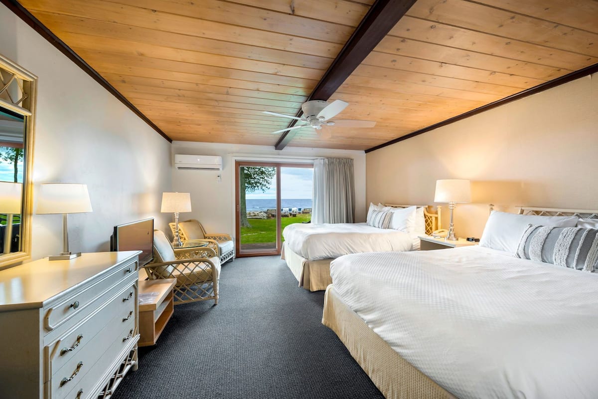 A hotel room with two beds, a desk, a chair, a dresser, and a ceiling fan.