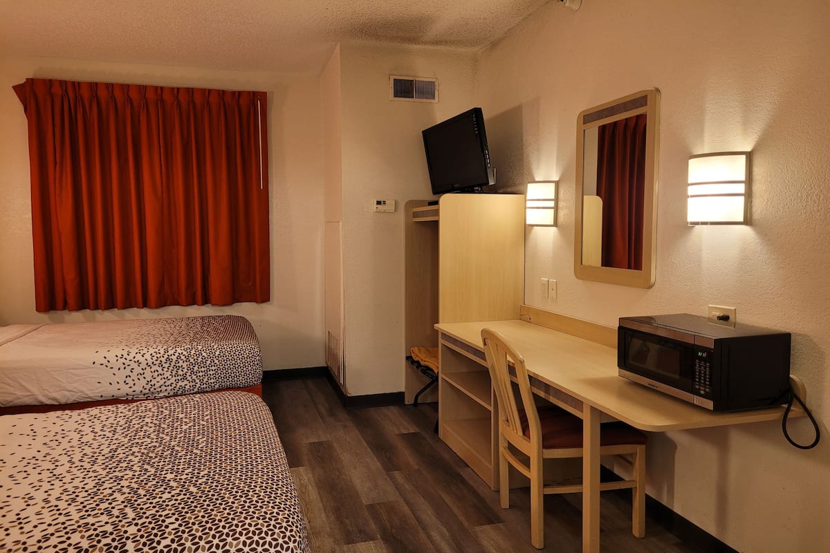 A hotel room with two beds, a desk with a chair, a television, a microwave, and a mirror.