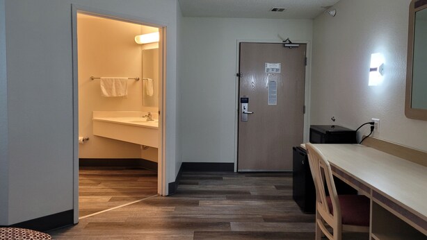 Une chambre d’hôtel avec un plancher en bois, un bureau avec une chaise, une petite poubelle et une porte dotée d’un interrupteur.