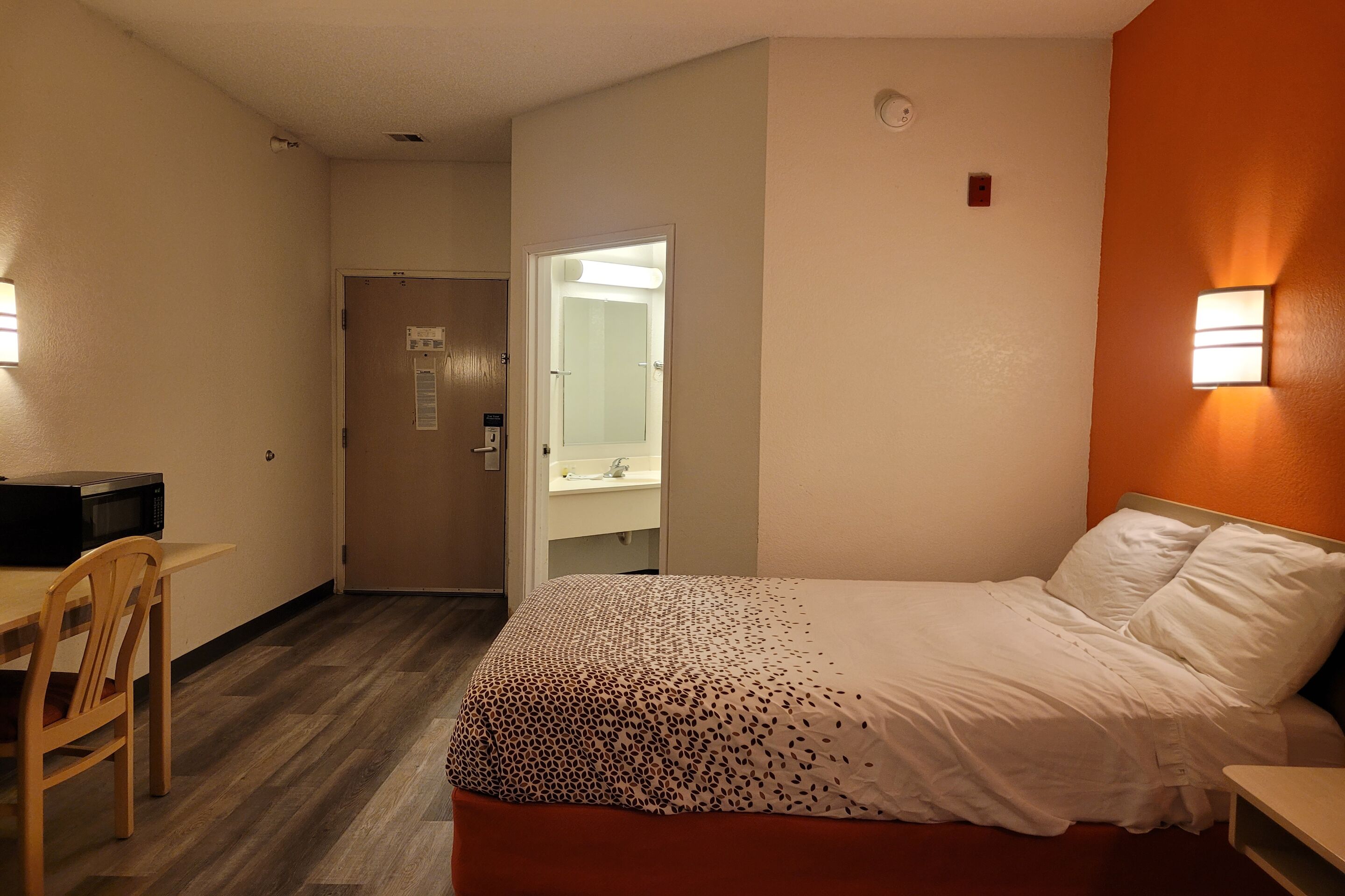 Habitació d'hotel amb llit, escriptori, cadira, bany i porta.
