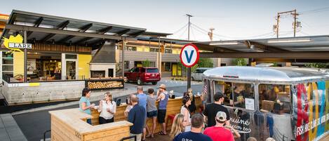 A street food truck with a colorful exterior and a sign advertising various activities. People are gathered around the truck, and a red SUV is parked nearby.