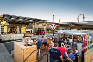 A street food truck with a colorful exterior and a sign advertising various activities. People are gathered around the truck, and a red SUV is parked nearby. - The LARK Bozeman (Bozeman)