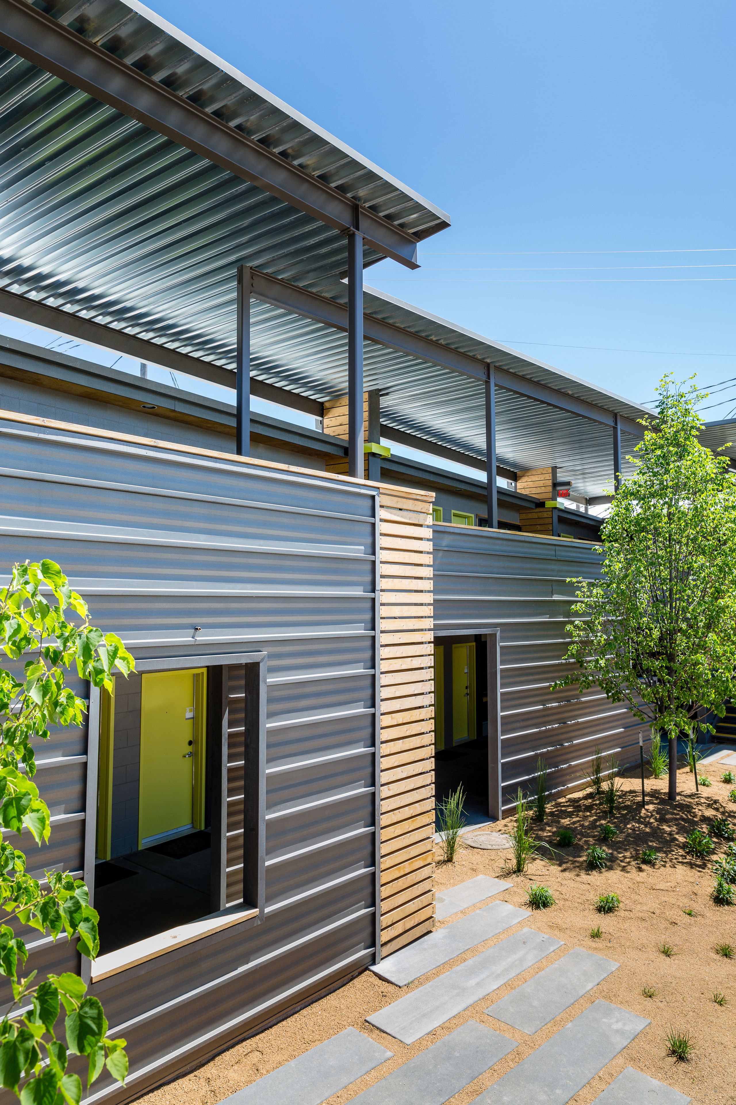 A modern building with a metal exterior, a covered outdoor area, and a small garden with stepping stones.